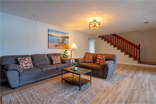 living area featuring a notable chandelier, light wood-style flooring, baseboards, visible vents, and stairway