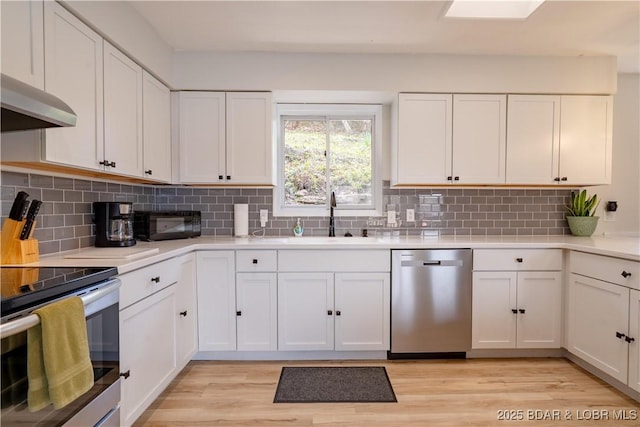 kitchen featuring appliances with stainless steel finishes, light wood-type flooring, a sink, light countertops, and white cabinets