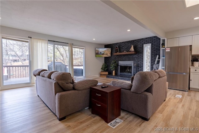living room with beamed ceiling, a brick fireplace, recessed lighting, and light wood-style flooring