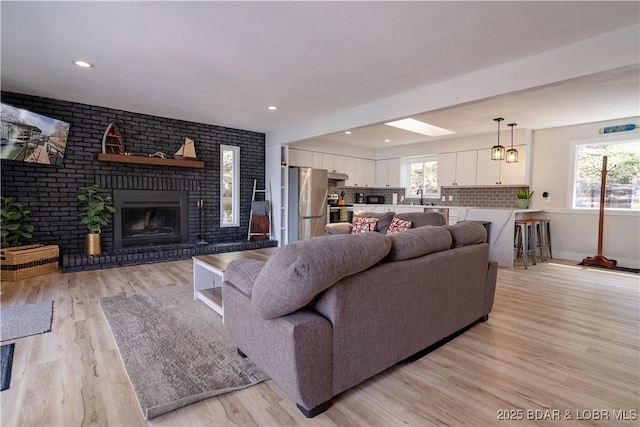 living area featuring plenty of natural light, light wood finished floors, a brick fireplace, and baseboards
