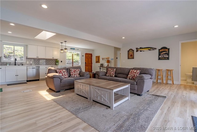 living room featuring a skylight, recessed lighting, and light wood-style flooring