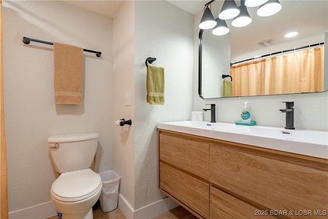 bathroom with double vanity, baseboards, and toilet