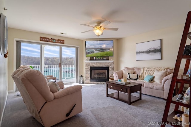 living area featuring ceiling fan, carpet, a stone fireplace, and visible vents
