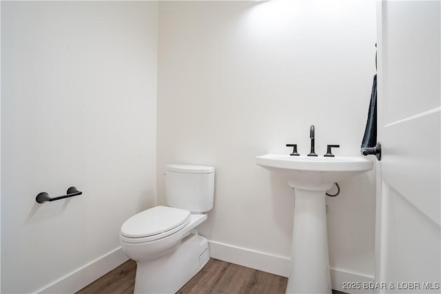 half bathroom featuring baseboards, wood finished floors, and toilet