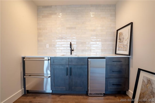 bar with dark wood-style flooring, a sink, baseboards, indoor wet bar, and stainless steel appliances