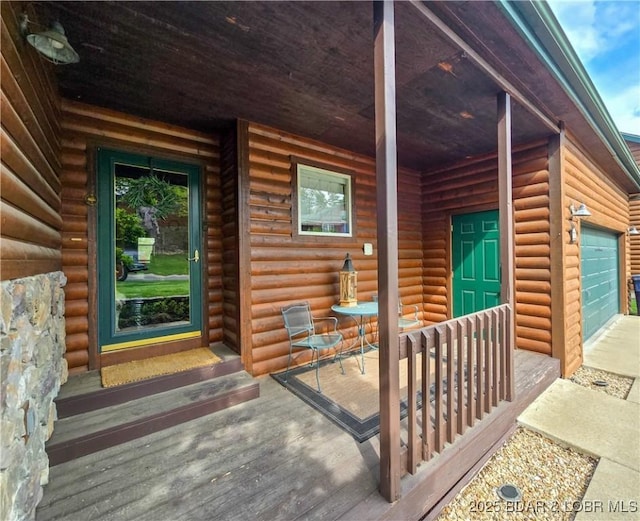 view of exterior entry with a porch, a garage, and log veneer siding