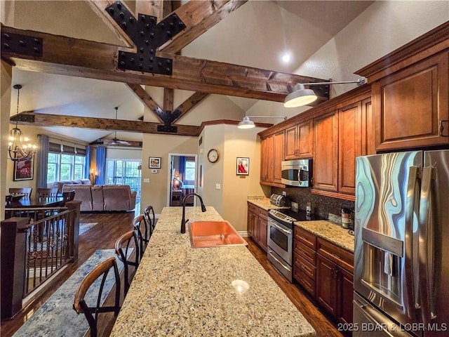 kitchen featuring appliances with stainless steel finishes, lofted ceiling with beams, a sink, a breakfast bar area, and dark wood finished floors