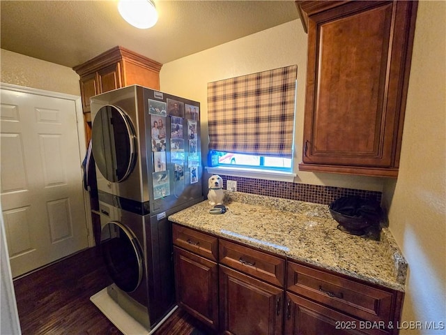clothes washing area featuring stacked washing maching and dryer, a textured wall, dark wood finished floors, and cabinet space