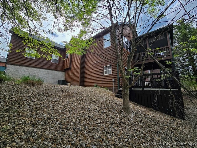 view of side of property featuring a wooden deck, faux log siding, a sunroom, and stairway