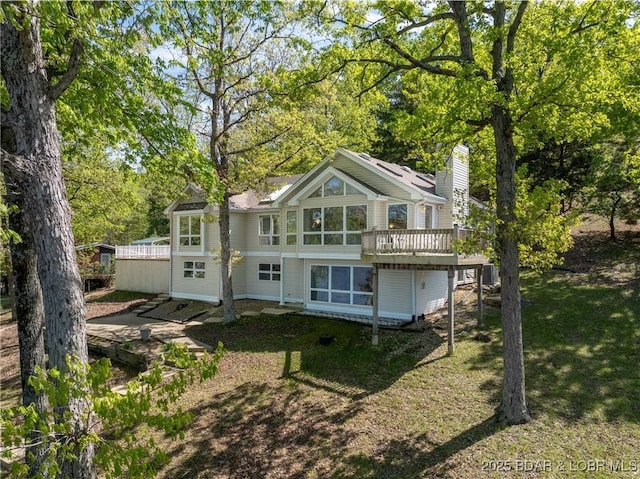 back of property featuring a lawn, a wooden deck, a chimney, and a sunroom