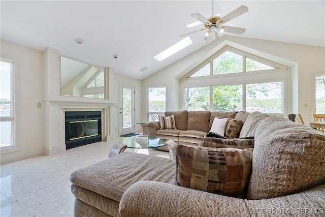 living room with high vaulted ceiling, a glass covered fireplace, a ceiling fan, baseboards, and a skylight