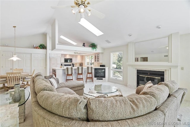 living area featuring a skylight, high vaulted ceiling, a fireplace, and a ceiling fan