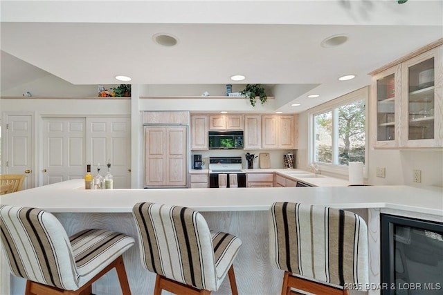 kitchen with a breakfast bar area, range with electric cooktop, black microwave, light brown cabinetry, and a peninsula