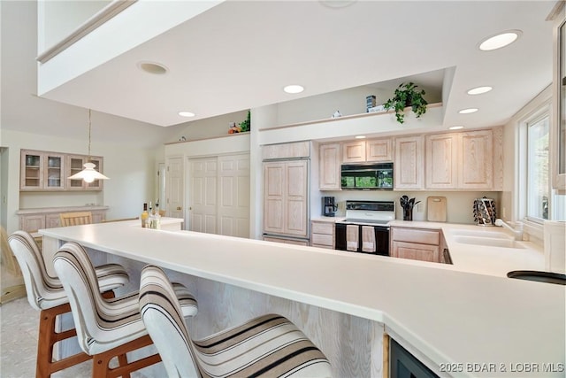 kitchen featuring a kitchen bar, black microwave, light brown cabinetry, a sink, and electric stove