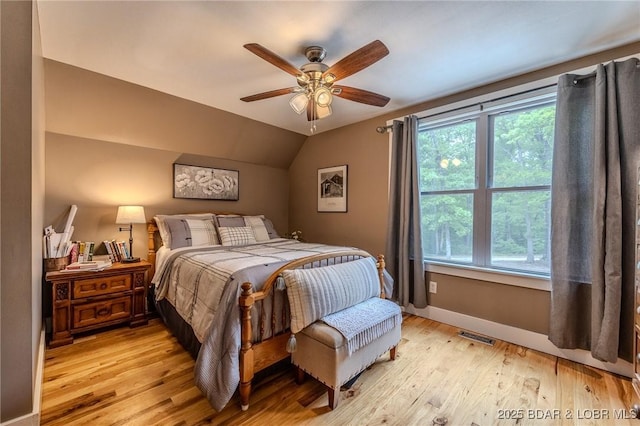 bedroom featuring light wood-style floors, baseboards, vaulted ceiling, and visible vents