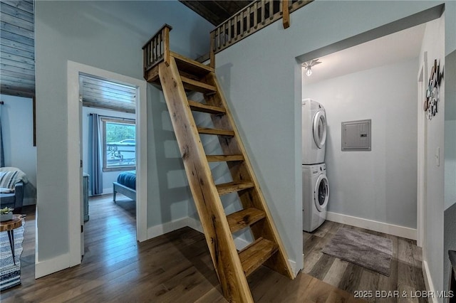 laundry area with laundry area, wood finished floors, baseboards, electric panel, and stacked washer / drying machine