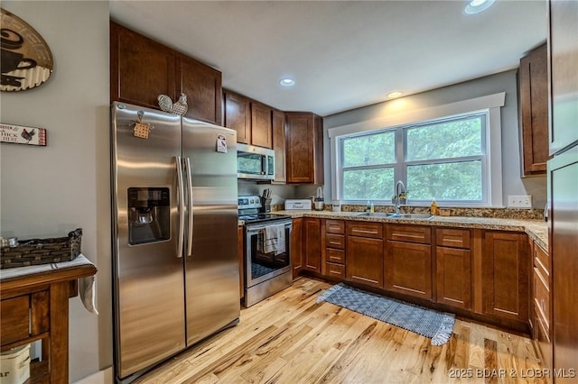 kitchen with a sink, light stone counters, light wood-style floors, stainless steel appliances, and recessed lighting