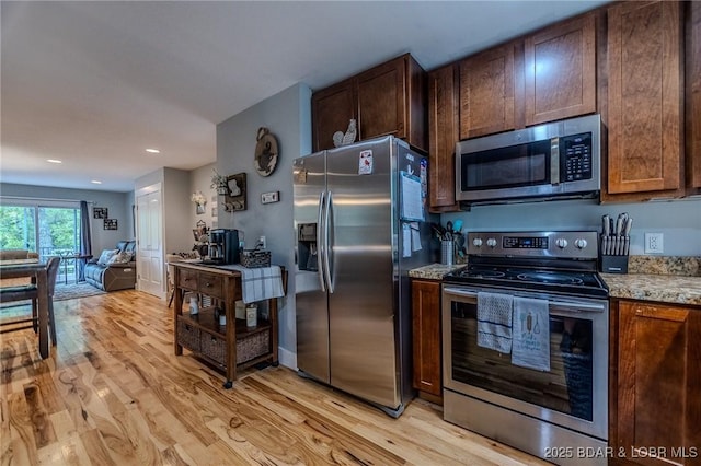 kitchen with open floor plan, light stone countertops, appliances with stainless steel finishes, and light wood-style flooring