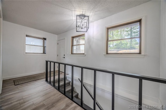 stairway with wood finished floors, baseboards, a textured ceiling, and a notable chandelier