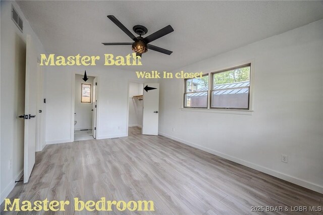 unfurnished bedroom with baseboards, a walk in closet, light wood finished floors, and visible vents