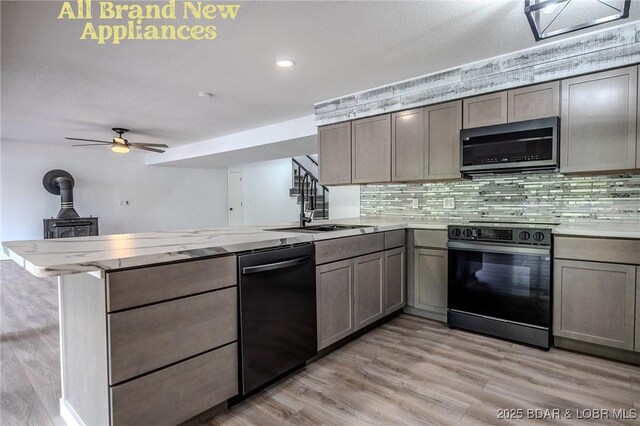 kitchen featuring a peninsula, light wood-style floors, black appliances, and tasteful backsplash