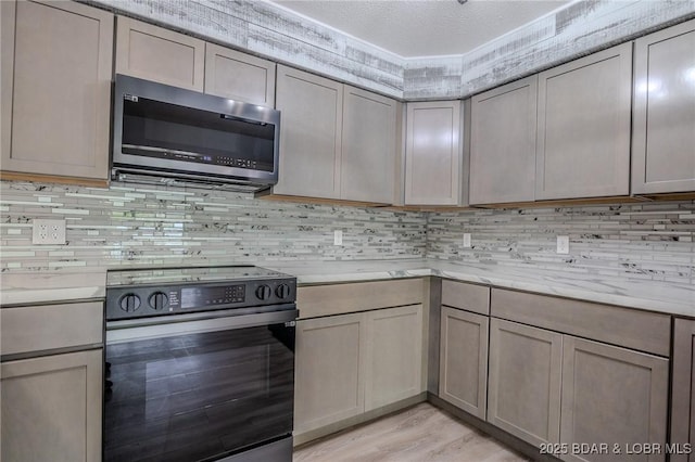 kitchen with light countertops, stainless steel microwave, tasteful backsplash, light wood-style flooring, and range with electric cooktop
