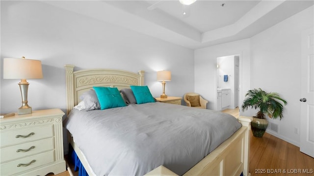 72 Emerald Bay Dr Unit 2D, Lake Ozark, MO 65049 - bedroom with ceiling fan, visible vents, a tray ceiling, ensuite bath, and light wood-style flooring