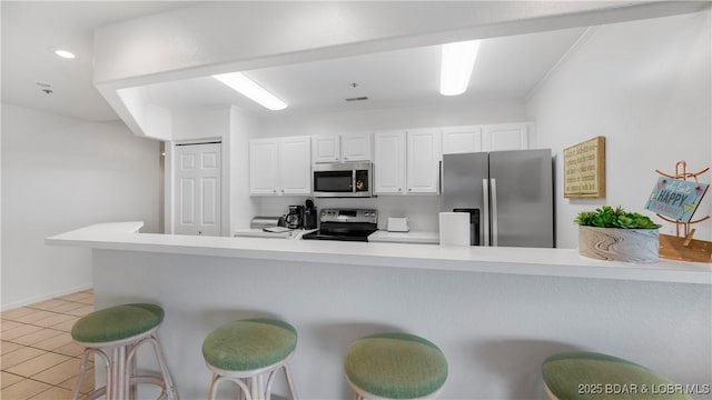 72 Emerald Bay Dr Unit 2D, Lake Ozark, MO 65049 - kitchen featuring light tile patterned flooring, appliances with stainless steel finishes, a breakfast bar, light countertops, and white cabinetry