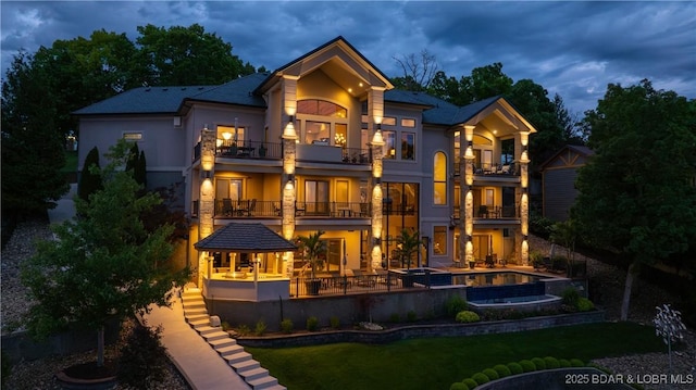 559 Forestridge Ln, Sunrise Beach, MO 65079 - rear view of house with a balcony, stucco siding, a pool with connected hot tub, and a patio