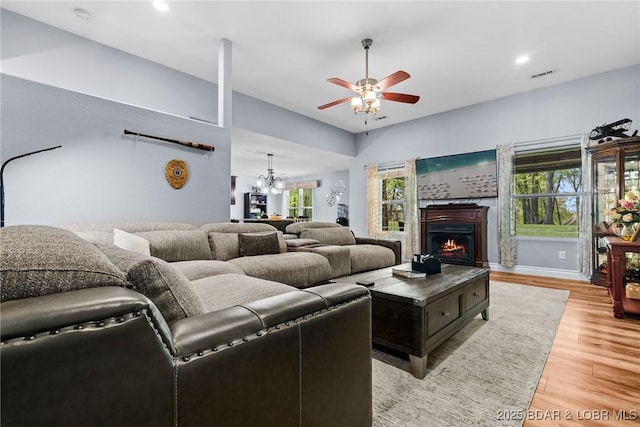 living area with a lit fireplace, visible vents, light wood-type flooring, ceiling fan with notable chandelier, and recessed lighting