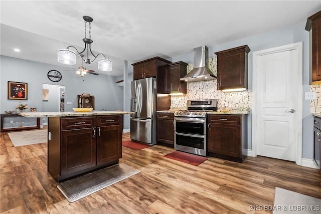 kitchen featuring dark brown cabinets, appliances with stainless steel finishes, light wood finished floors, wall chimney exhaust hood, and decorative backsplash