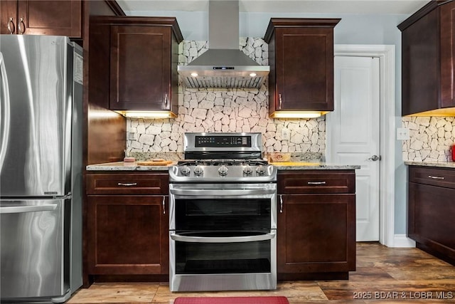 kitchen with wall chimney range hood, appliances with stainless steel finishes, tasteful backsplash, and light stone counters