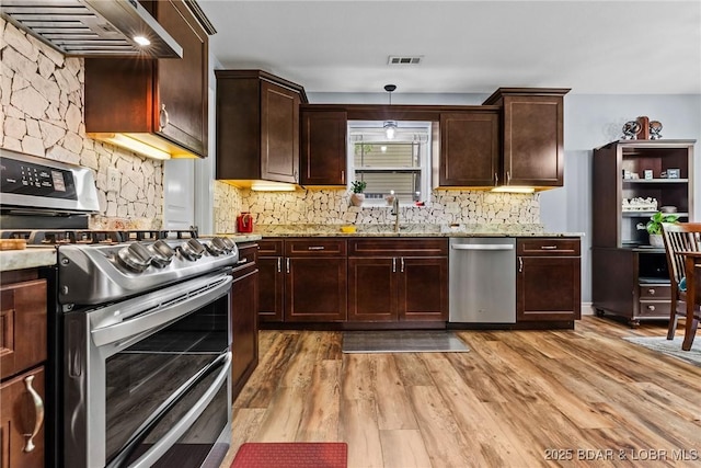 kitchen with wall chimney exhaust hood, tasteful backsplash, light stone counters, a sink, and stainless steel appliances