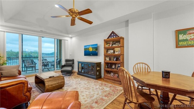 living area featuring ceiling fan, wood finished floors, and a tray ceiling