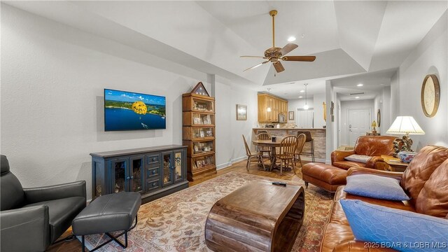 living area with baseboards, ceiling fan, wood finished floors, and vaulted ceiling