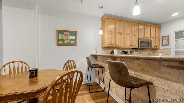 kitchen featuring light brown cabinetry, stainless steel microwave, wood finished floors, tasteful backsplash, and pendant lighting