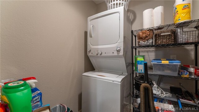 laundry room with laundry area, a textured wall, and stacked washer / dryer
