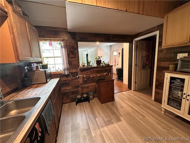 kitchen with wood walls, a sink, light countertops, stainless steel microwave, and light wood-style floors