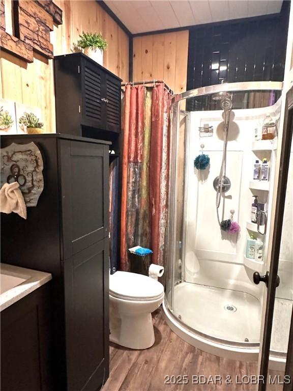 bathroom with wood walls, wood finished floors, toilet, and a shower stall