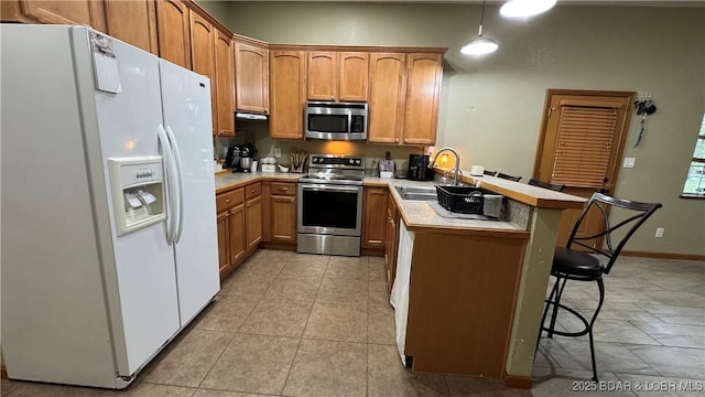 kitchen featuring a kitchen breakfast bar, appliances with stainless steel finishes, a sink, light countertops, and a peninsula