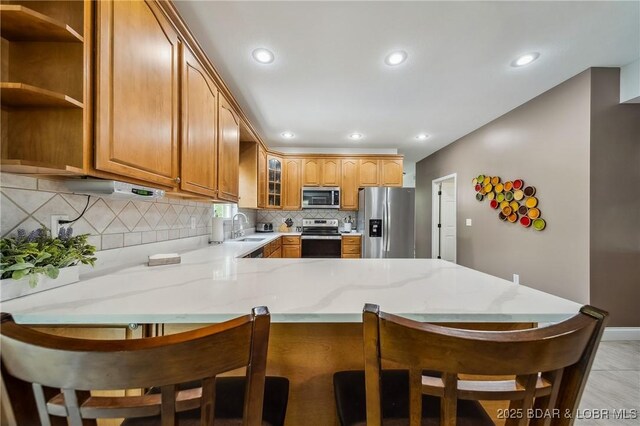 kitchen with light stone countertops, appliances with stainless steel finishes, a sink, a peninsula, and tasteful backsplash