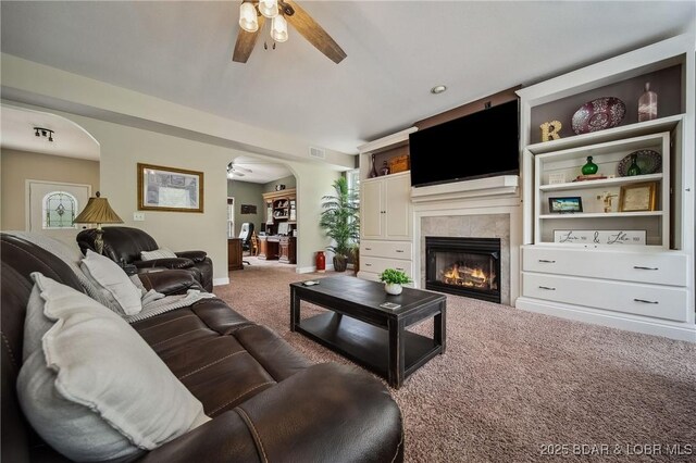 living area with carpet floors, visible vents, a fireplace, ceiling fan, and arched walkways