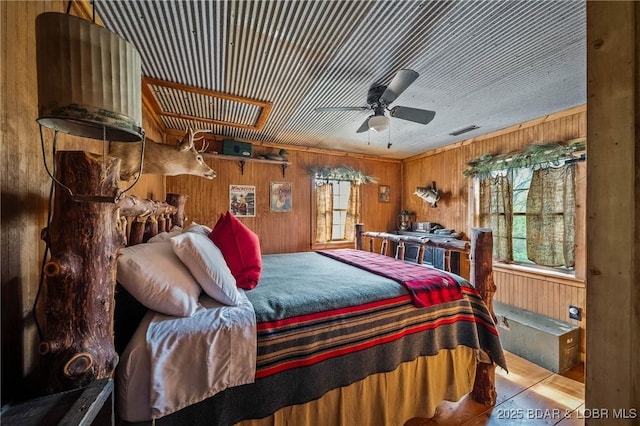 bedroom with wooden walls, wood finished floors, visible vents, and multiple windows