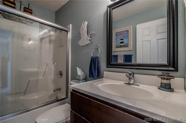 bathroom with vanity, a textured wall, enclosed tub / shower combo, and toilet