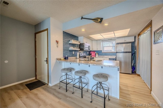 256 Lone Oak Pt Unit 15, Sunrise Beach, MO 65079 - kitchen featuring open shelves, a peninsula, a textured ceiling, light wood-style flooring, and appliances with stainless steel finishes