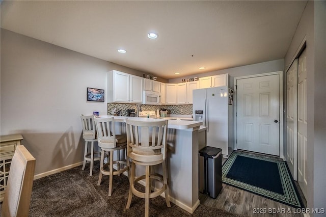 kitchen with white appliances, baseboards, a kitchen bar, light countertops, and white cabinetry