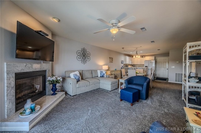 living room featuring a premium fireplace, a ceiling fan, and dark colored carpet