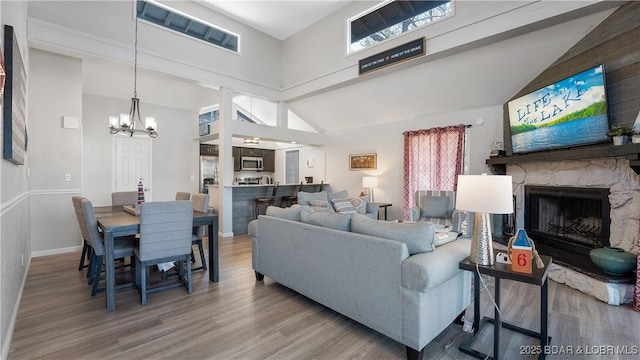 living area featuring high vaulted ceiling, a chandelier, a stone fireplace, and wood finished floors