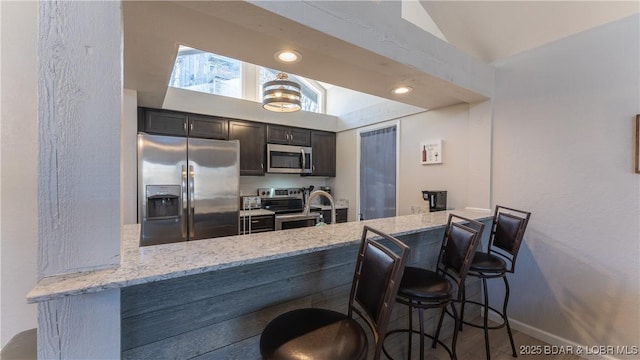 kitchen with a peninsula, light stone countertops, appliances with stainless steel finishes, and lofted ceiling