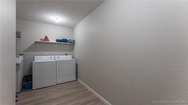 laundry area with laundry area, a textured ceiling, washing machine and dryer, wood finished floors, and baseboards